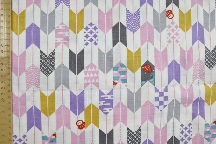 Japanese arrow feather yagasuri fabric pink and mauve on a white background, flat with ruler